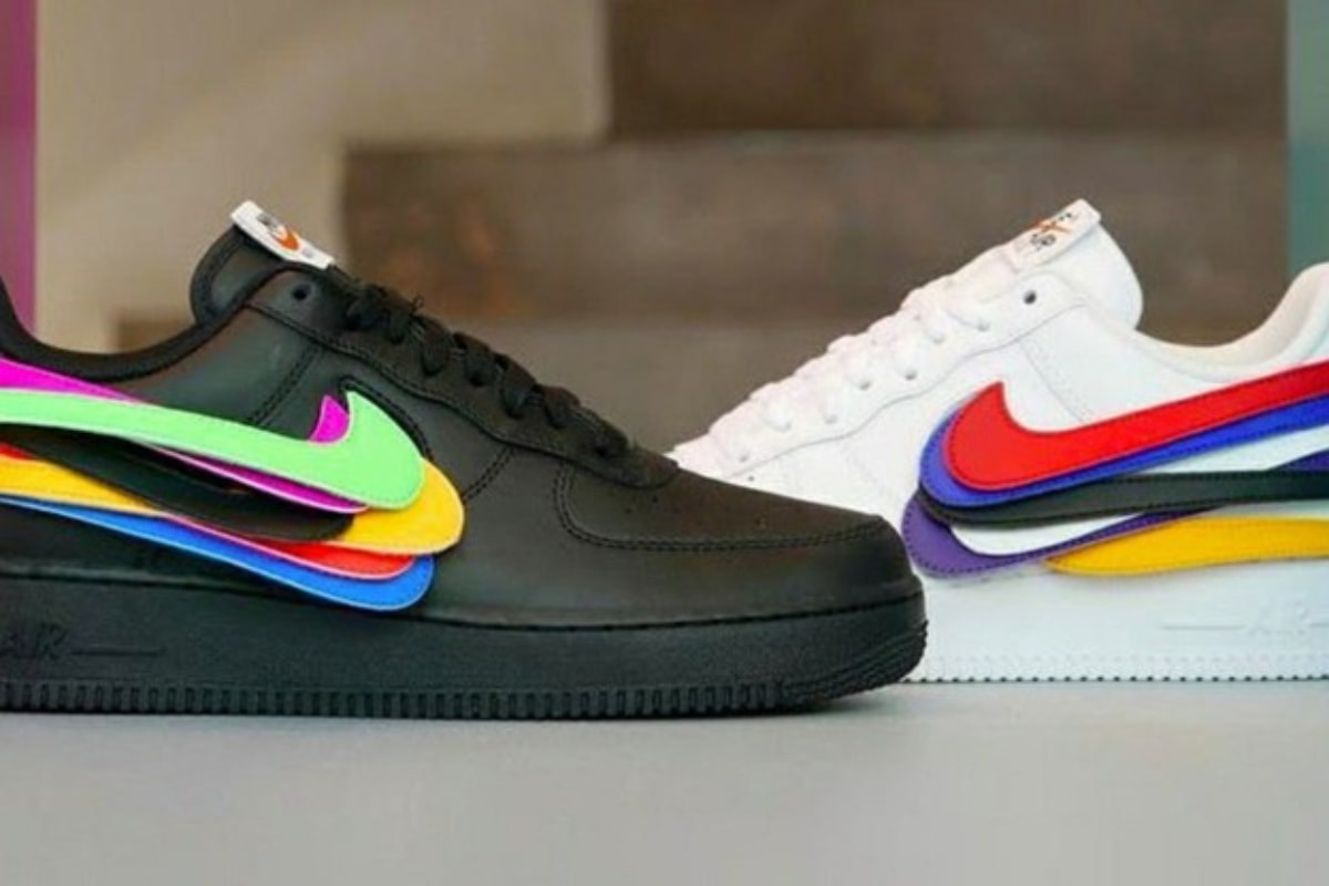 A pair of black and white Nike Air Force 1 sneakers featuring interchangeable multi-colored swoosh logos attached using customizable Hook and Loop Straps.