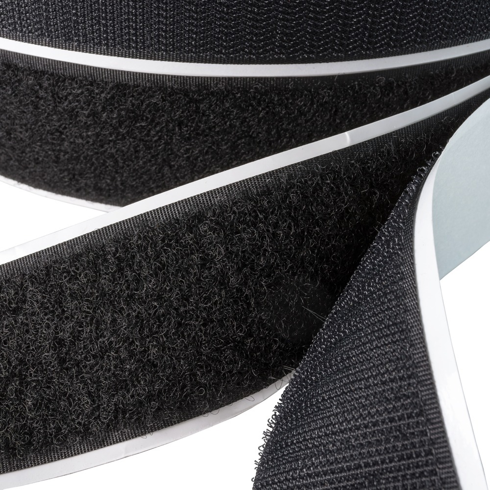 A close-up macro view of black DuraGrip pressure-sensitive loop material with a rubber-based adhesive backing being unrolled for manufacturing Hook and Loop Straps.