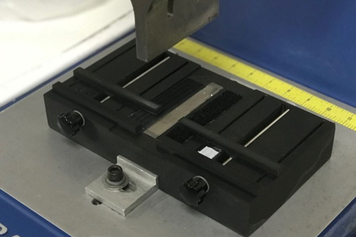 A close-up view of the black alignment fixture bed located directly beneath the ultrasonic horn of the welding machine.
